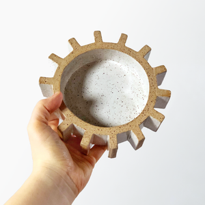 sculptural gear or cog tray being held by hand on plain background